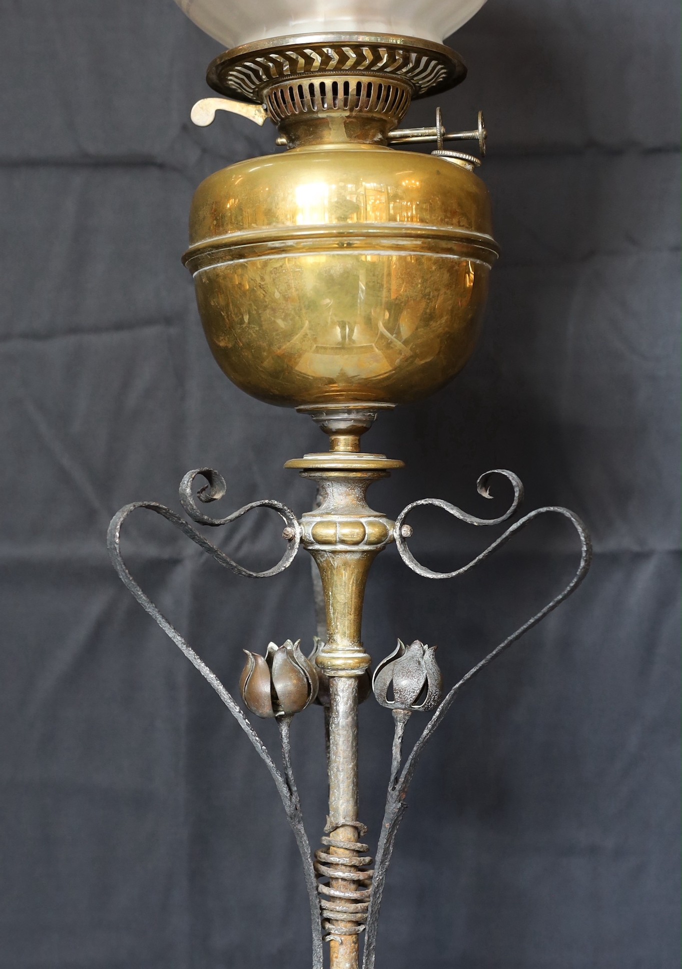 A late Victorian Arts and Crafts wrought iron and brass miniature oil lamp standard, in the manner of Benson, with duplex mechanism and later cranberry tinted glass shade, height without shade 96cm.